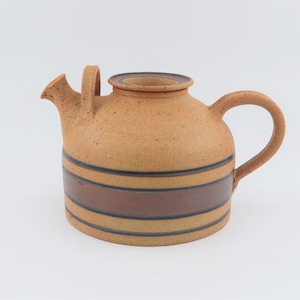 May include: A brown ceramic teapot with a speckled glaze and brown stripes. The teapot has a rounded body and a spout on one side.