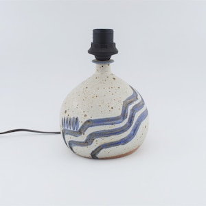 May include: A white ceramic table lamp with blue and grey wavy lines. The lamp has a black cord and switch.