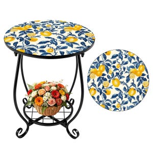 May include: A round side table with a black metal frame and a lemon-themed tabletop. The table has a decorative shelf holding a basket of flowers. The tabletop has a white background with yellow lemons and blue leaves.