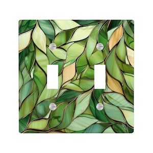 May include: A square double light switch wall plate featuring a stained glass pattern of overlapping leaves in various shades of green, light yellow, and cream, separated by dark brown lines, with four silver screws securing the plate.