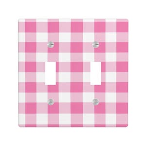 Könnte beinhalten: Eine doppelte Lichtschalterabdeckung mit einem rosa-weißen Vichy-Muster. Sie hat zwei rechteckige Aussparungen für die Schalter und vier silberne Schrauben. Das Design ist ein klassischer, fröhlicher Stil.