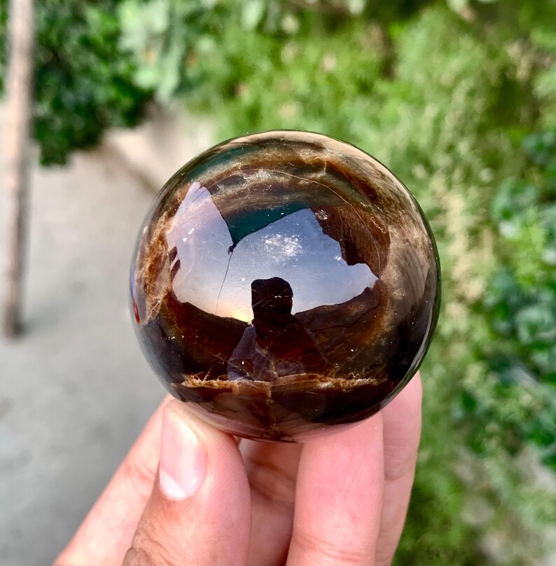 May include: A smooth, dark brown sphere with a shimmering, iridescent finish. The sphere is made of natural stone and has a unique, swirling pattern.