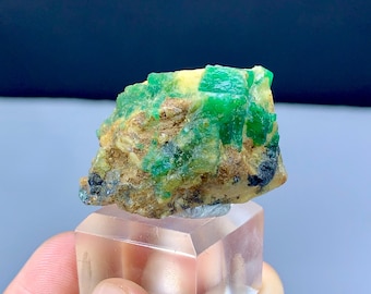 May include: A rough, green emerald specimen with a cluster of crystals embedded in a brown matrix. The emerald is a vibrant green color and has a glassy luster.