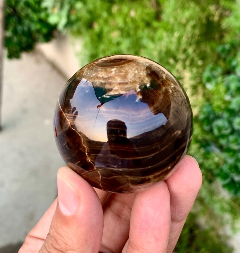 May include: A polished brown and black sphere with swirling patterns. The sphere is made of natural stone and has a smooth, glossy finish.
