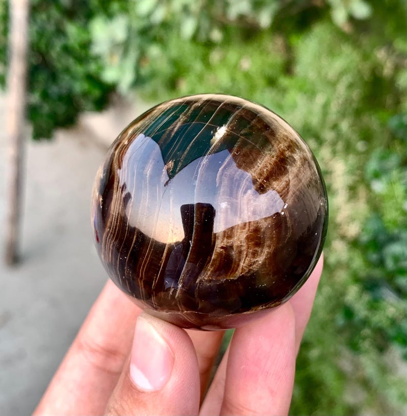 May include: A polished, dark brown and black sphere with swirling patterns. The sphere is made of natural stone and has a high gloss finish.