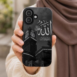 Peut inclure: Coque de téléphone noire avec une image en niveaux de gris d'une tour d'horloge et de bâtiments, avec de la calligraphie arabe blanche. La coque a une découpe pour l'appareil photo et une finition lisse.