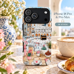 Könnte beinhalten: Eine Handyhülle für iPhone 18 Pro und Pro Max mit einer Illustration der Kaaba in Mekka, umgeben von Topfpflanzen, einer Kaffeetasse mit Herz und einem kleinen Smartphone. Der Text lautet iPhone 18 Pro & Pro Max IN STOCK.