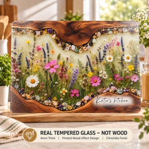 May include: A rectangular tempered glass cutting board featuring a printed wood-effect border and a central meadow design with pressed wildflowers, greenery, and small stones. The text Katie's kitchen is printed in black script on the lower right.