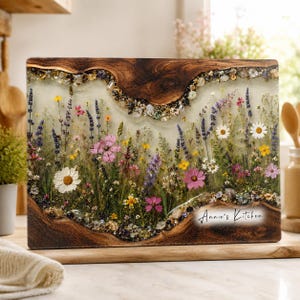 May include: A rectangular wooden serving board featuring a central section of clear resin embedded with dried wildflowers, lavender, and small crystals. The wood has a natural live edge, and the text Annie's Kitchen is printed in black.