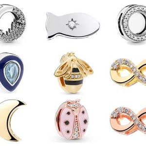 May include: A collection of jewelry charms in various designs. Includes a silver charm with a cityscape design, a silver fish-shaped charm with a central gem, and a silver charm with a circle of clear stones. Other charms include a blue teardrop, a gold bee, and infinity symbols.