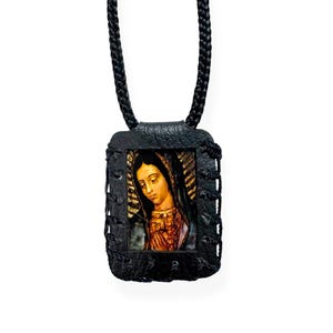 May include: Black leather pendant necklace with a picture of the Virgin Mary inside. The pendant is rectangular and has a braided cord.