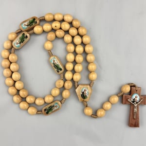 May include: A wooden rosary with light brown beads and a brown wooden cross. The rosary features painted images of religious figures on some of the beads and the cross. The beads are connected by a woven cord.