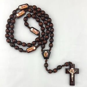 May include: A dark brown wooden rosary with oval beads and rectangular decorative pieces featuring religious imagery. The rosary includes a crucifix with a silver-toned Jesus figure and a central pendant with a saint illustration.