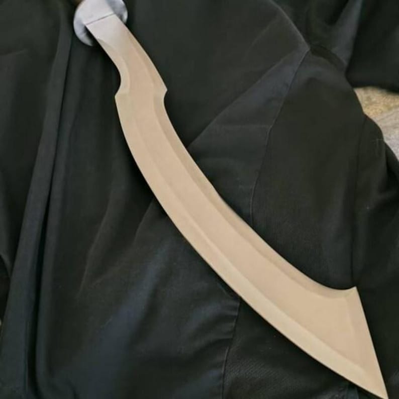 May include: A curved, tan-colored sword with a silver handle. The blade has a distinctive, crescent shape. The sword is lying on a dark, textured surface.