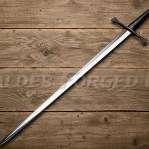 May include: A long, silver sword with a black handle and crossguard, resting on a wooden surface. The blade is sharp and pointed, and the handle has a rounded pommel. The text "BALDES FORGED US" is faintly visible on the wood.