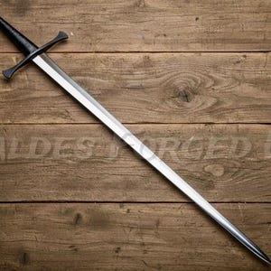 May include: A long, silver sword with a black handle and crossguard, resting on a wooden surface. The blade is polished and reflects light, while the handle and crossguard have a matte finish. The sword is a historical weapon.