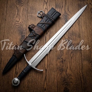 May include: A long, silver sword with a black handle and a rounded pommel, resting beside its leather sheath. The sheath is black and brown, with intricate straps and a buckle. The text "Titan Sharp Blades" is visible.