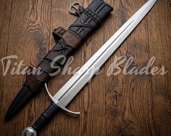 Peut inclure: Une longue épée argentée avec une poignée noire et un pommeau arrondi, posée à côté de son fourreau en cuir. Le fourreau est noir et marron, avec des sangles et une boucle. Le texte "Titan Sharp Blades" est visible.