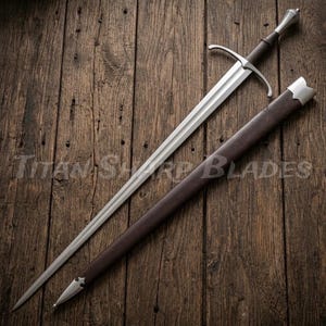 May include: A long, silver sword with a brown handle and a matching sheath. The sword has a cross-shaped hilt and a pointed tip. The sheath is dark brown with silver accents. The text "Titan Sharp Blades" is visible.