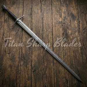 May include: A long, silver sword with a black handle and crossguard, resting on a wooden surface. The blade has a textured appearance. The text "Titan Sharp Blades" is visible on the wooden surface.