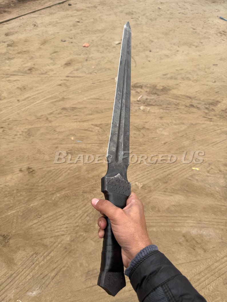 May include: A long, dark metal dagger with a pointed tip and a textured handle. The blade has a central ridge and is held in a hand. The text "BLADES FORGED US" is visible on the image.