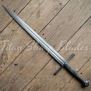 Peut inclure: Une longue &eacute;p&eacute;e argent&eacute;e avec une garde en forme de croix et un pommeau arrondi. La lame est tranchante et effil&eacute;e, et le manche est gris fonc&eacute;. L'&eacute;p&eacute;e est pr&eacute;sent&eacute;e sur une surface en bois, avec le texte "Titan Blades".