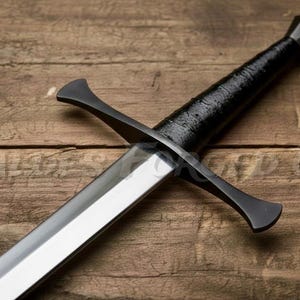 May include: A medieval-style sword with a polished steel blade and a black handle wrapped in textured material. The crossguard and pommel are also black. The sword rests on a wooden surface.