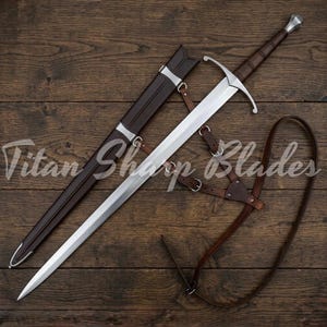 May include: A long, silver sword with a brown handle and a leather sheath. The sword has a crossguard and is accompanied by a brown leather belt. The text "Titan Sharp Blades" is visible.