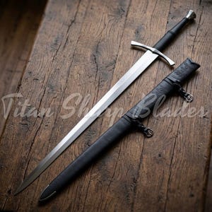 May include: A long, silver sword with a black handle and crossguard, on a wooden surface. A black sheath with decorative tooling is next to the sword. The text "Titan Shop Blades" is visible.