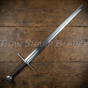May include: A long steel sword featuring a double-edged blade, a straight metal crossguard, a dark cylindrical grip, and a round pommel. The blade has a central fuller running down its length. The text TITAN SHARP BLADES is visible.