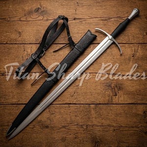 Peut inclure: Une longue épée argentée avec une poignée et une garde noires, dans un fourreau noir. Une sangle en cuir noir est à gauche. Le texte "Titan Sharp Blades" est visible.