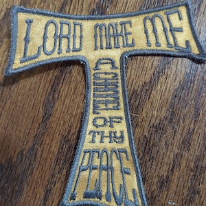 May include: A gold-colored fabric patch in the shape of a cross with the words "Lord Make Me A Channel Of Thy Peace" embroidered in black thread.