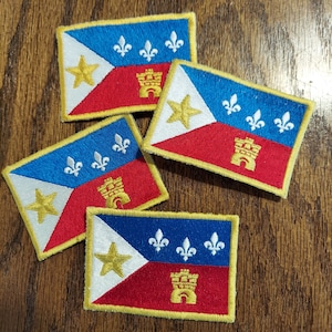May include: Four embroidered patches featuring the flag of New Orleans, Louisiana. Each patch is rectangular and features a white background with a red and blue design. The patches are surrounded by a gold border.