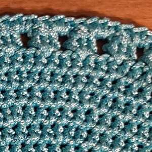 May include: A close-up of a teal crocheted doily with a scalloped edge and small holes throughout the design.