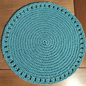 May include: A teal crocheted placemat with a circular design and a scalloped edge.
