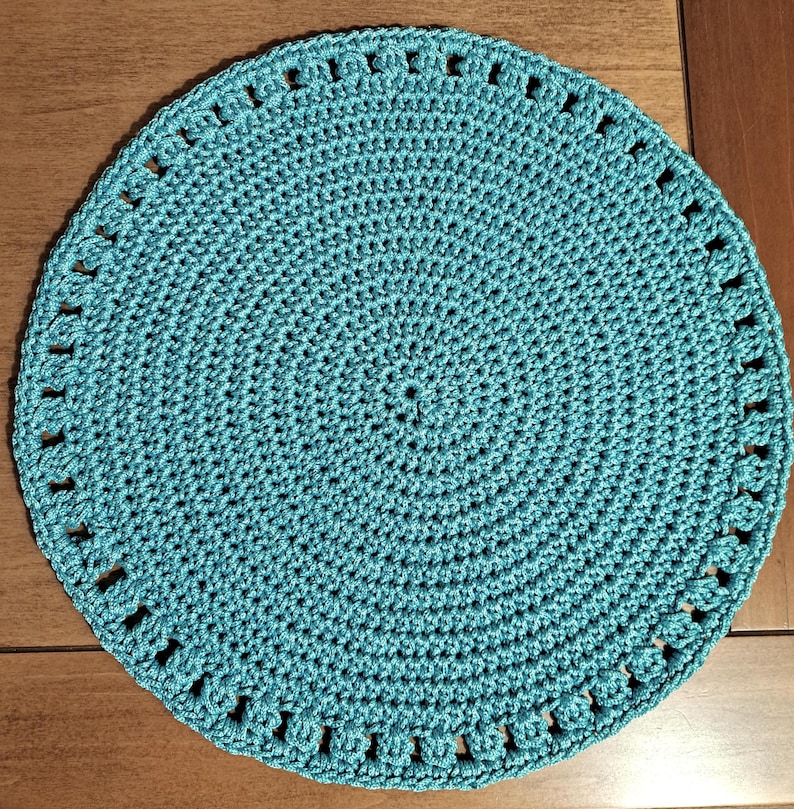 May include: A teal crocheted placemat with a circular design and a scalloped edge.