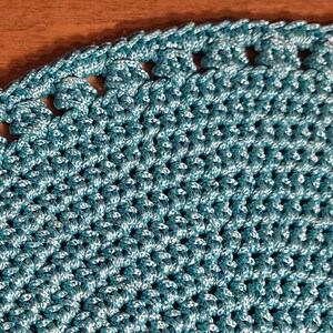 May include: A teal blue crocheted doily with a scalloped edge.