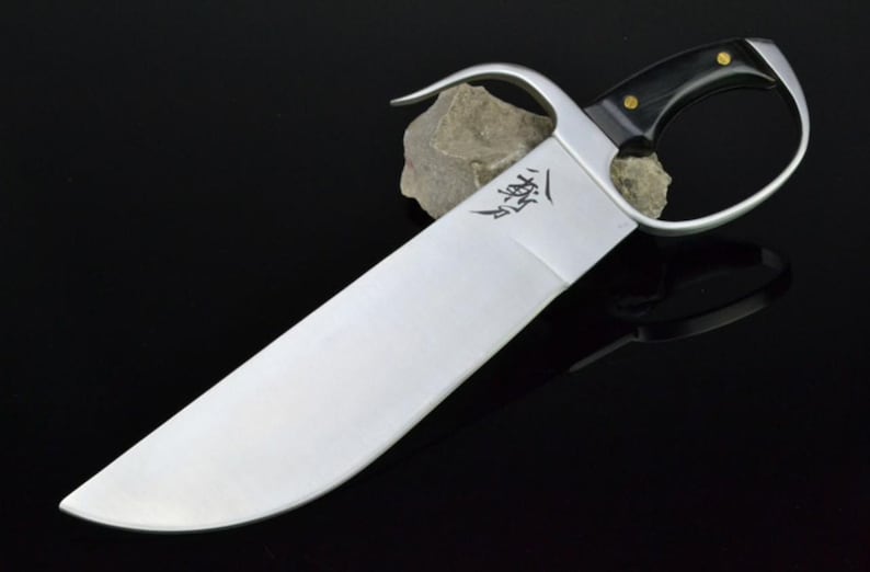 May include: A silver-colored Kung Fu sword with a black handle and gold accents. The sword has a curved blade and a ring handle.