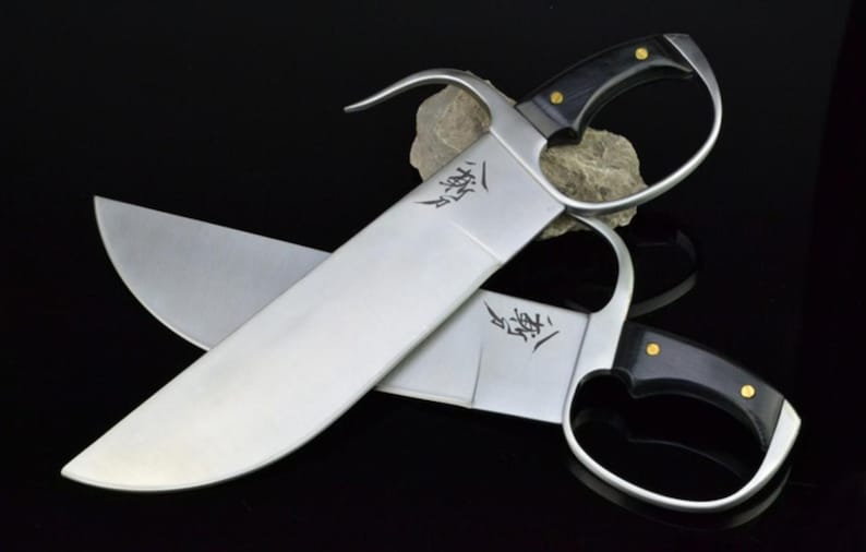 May include: Two silver-colored Kung Fu swords with black handles. The swords are crossed and the blades have Chinese characters inscribed on them.