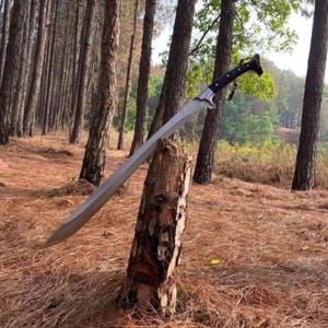May include: A long, silver sword with a black handle is propped against a tree stump in a forest setting. The sword has a sharp point and a curved blade.