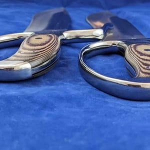 Peut inclure: Une paire de grands ciseaux en m&eacute;tal brillant avec des poign&eacute;es en bois. Les poign&eacute;es pr&eacute;sentent un motif de grain de bois brun clair et brun fonc&eacute;. Les lames sont incurv&eacute;es.