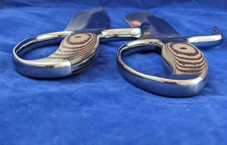 Peut inclure: Une paire de grands ciseaux en m&eacute;tal brillant avec des poign&eacute;es en bois. Les poign&eacute;es pr&eacute;sentent un motif de grain de bois brun clair et brun fonc&eacute;. Les lames sont incurv&eacute;es.