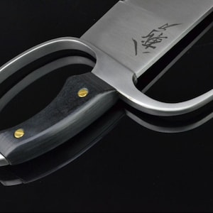 May include: A silver-colored Kung Fu sword with a black wooden handle and two brass accents. The blade has a curved handle and a sharp point. The blade is engraved with Chinese characters.