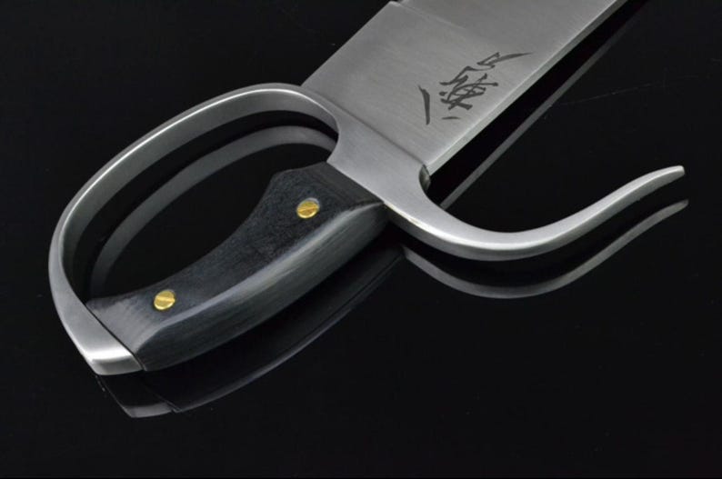 May include: A silver-colored Kung Fu sword with a black wooden handle and two brass accents. The blade has a curved handle and a sharp point. The blade is engraved with Chinese characters.