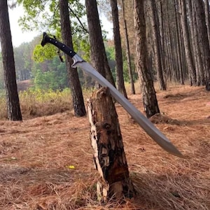 May include: A long, silver sword with a black handle is propped against a tree stump in a forest setting. The sword has a sharp point and a curved blade.