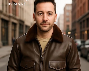 Puede incluir: Chaqueta bomber de cuero marrón con cuello de piel, dos bolsillos delanteros y cierre de cremallera. La chaqueta se lleva con un jersey de color claro y vaqueros azules. El texto "Clothing BY MAAZ" está en la parte superior izquierda.