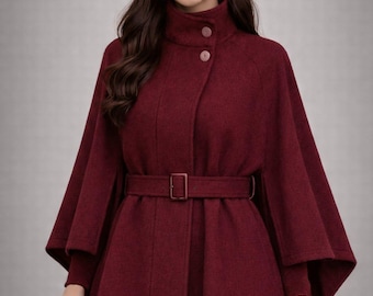 May include: A burgundy cape coat with a high collar and a matching belt. The coat features a button closure and flared sleeves. The overall style is elegant and suitable for cooler weather.