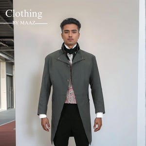 以下が含まれることがあります： ハイカラーのグレーのロングコート。柄入りのベストと白いシャツの上に着用。黒いパンツと靴でコーディネートされています。画像には「Clothing by MAAZ」の文字が含まれています。