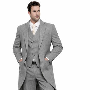 May include: A three-piece gray suit with a long tailcoat, vest, and trousers. The suit is paired with a white dress shirt and a patterned tie. The man is wearing black dress shoes.