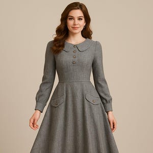 May include: A gray, long-sleeved dress with a round collar and button details. The dress features two front pockets and a flared skirt. The model is wearing beige heels. The dress is a classic, vintage style.